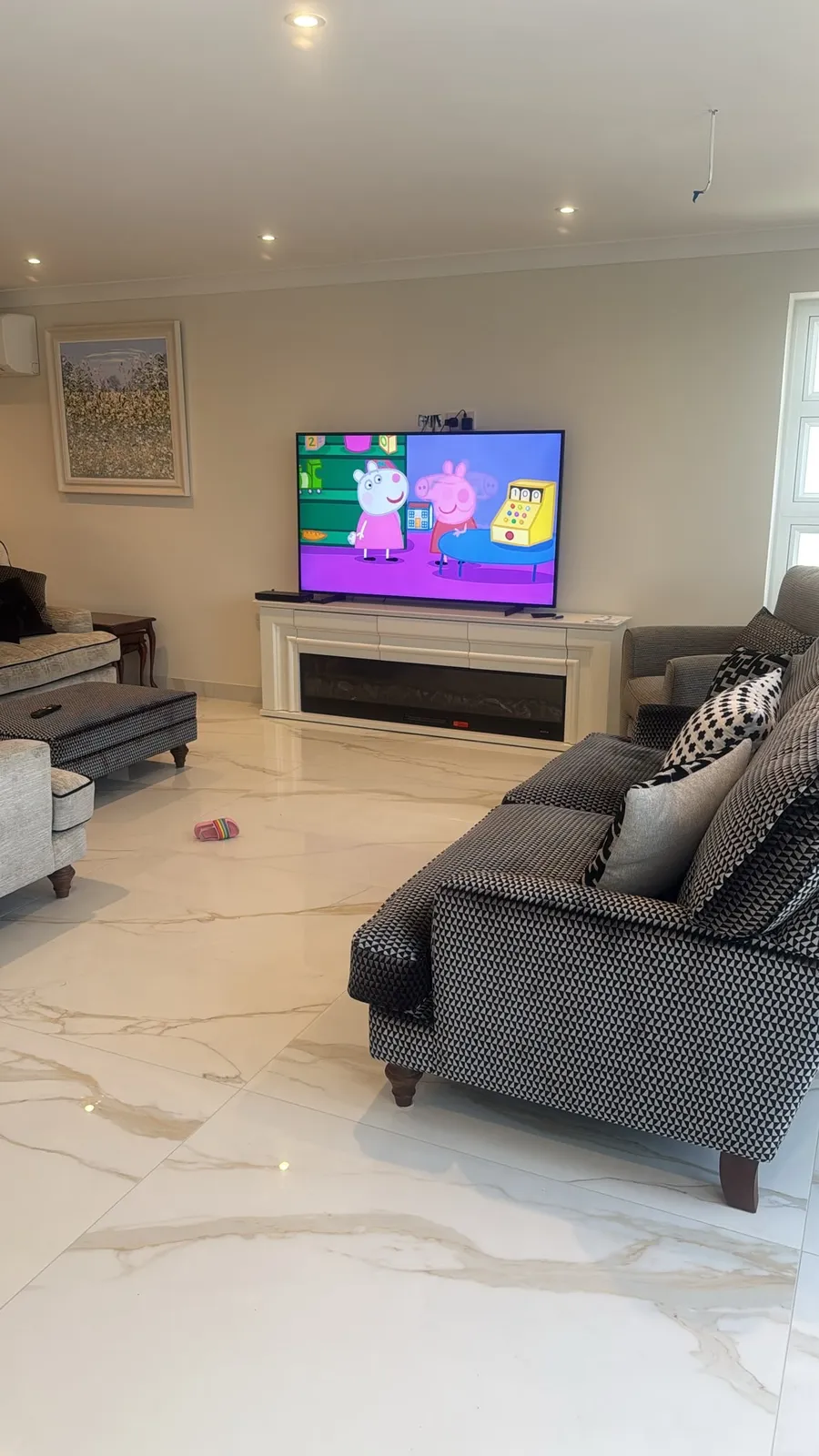 Before: a plain painted living room wall with the TV sat on top of a freestanding fireplace mantel and sockets visible above it