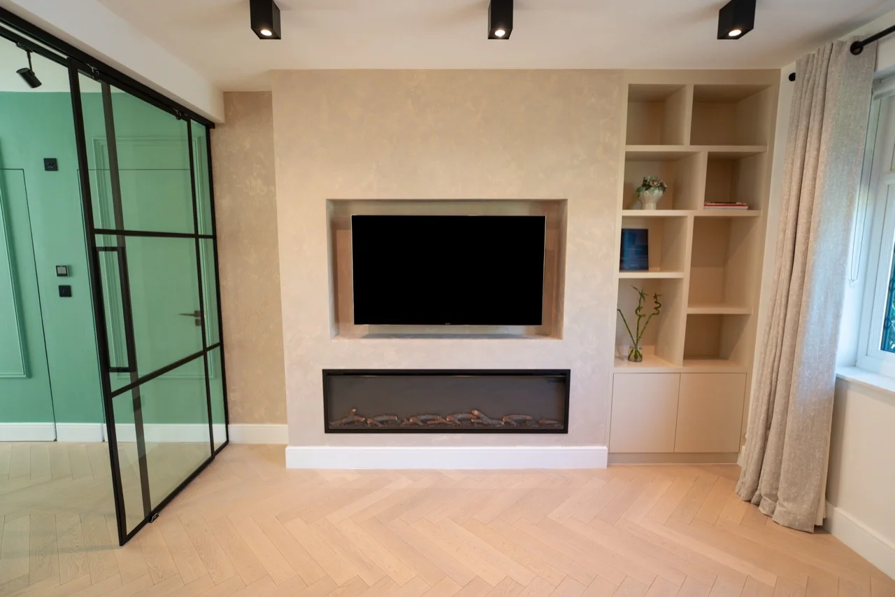 Completed media wall with visible clearance around a recessed TV, a fireplace below and fitted shelving to the right